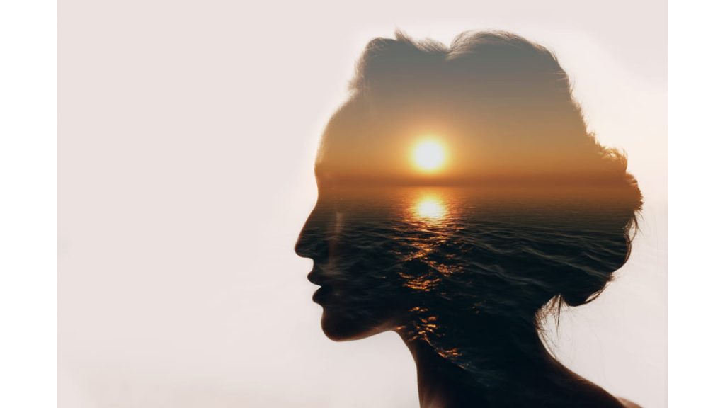 Picture of a silhouette of a woman's face with a sunset coastal scene overlay