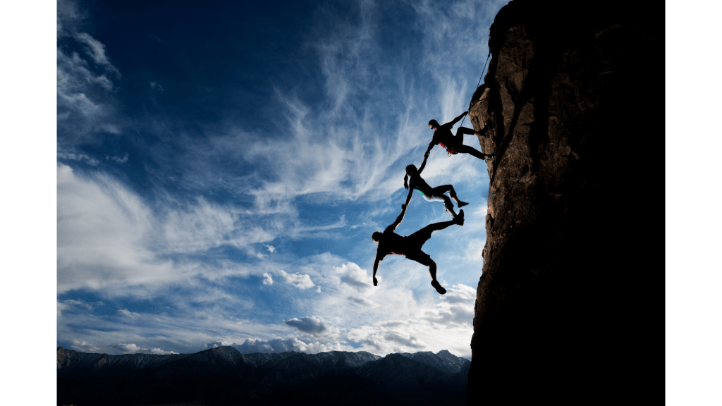 Photo of three people holding on to each other as they climb a steep cliff