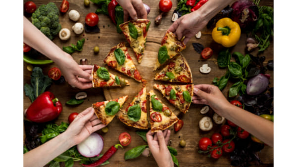 Picture of a large pizza on a table with hands reaching out to grab slices